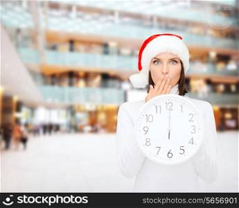 christmas, time, winter and people concept - smiling woman in santa helper hat with clock showing 12 over shopping center background