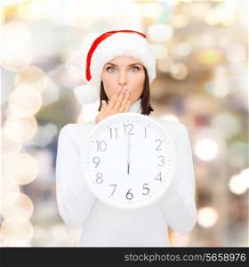 christmas, time, winter and people concept - smiling woman in santa helper hat with clock showing 12 over lights background