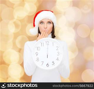 christmas, time, winter and people concept - smiling woman in santa helper hat with clock showing 12 over beige lights background