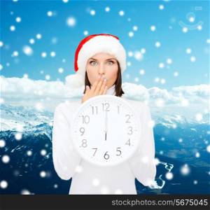 christmas, time, winter and people concept - smiling woman in santa helper hat with clock showing 12 over snowy mountains background