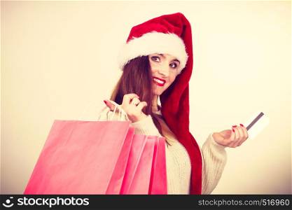 Christmas time. Young latin woman wearing santa claus hat holding red shopping bags and credit card, buying gifts. woman in Christmas hat holds credit card and shopping bags.