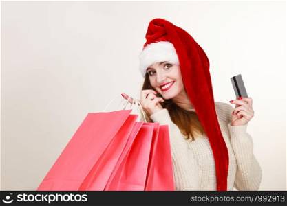 Christmas time. Young latin woman wearing santa claus hat holding red shopping bags and credit card, making gifts