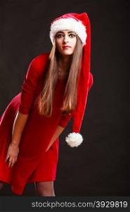 Christmas time. Young woman wearing santa claus hat red dress on black background. Studio shot.