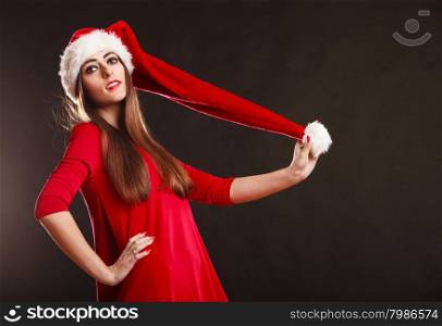 Christmas time. Young woman wearing santa claus hat red dress on black background. Studio shot.