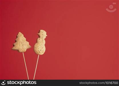 Christmas tree and snowman shape cookies on skewers, on red background. Xmas traditional gingerbread cookies. American Christmas famous dessert.