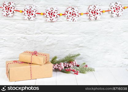 Christmas tree branch and gift boxes in craft paper with red bow on white brick wall background with snowflakes garland. New Year background with copy space, wallpaper, greeting card