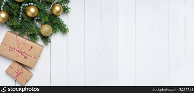 Christmas tree branch decorated with golden balls and gift boxes with in craft paper on white wooden background. Top view, flat lay with copy space, banner, header, New Year background. Christmas background with decorated fir tree and gift boxes. Top view, flat lay with copy space