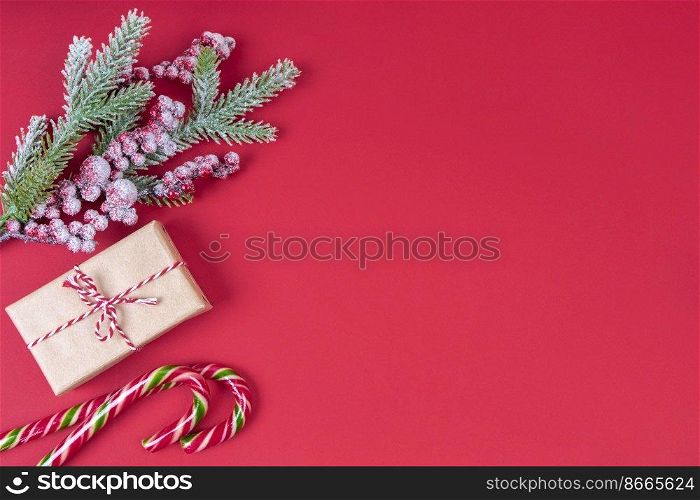 Christmas tree branch decorated with snow and berries, gift box and candy cane on red background. Top view, flat lay with copy space, banner, header, New Year background