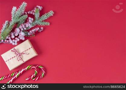Christmas tree branch decorated with snow and berries, gift box and candy cane on red background. Top view, flat lay with copy space, banner, header, New Year background