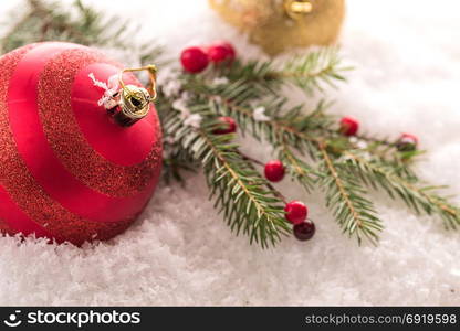 Christmas tree branch, red berries and red ball on snow