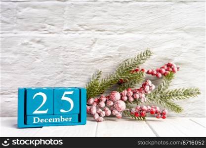Christmas tree branch with red berries and blue perpetual calendar with date 25 december on white brick wall. Banner, header, New Year background