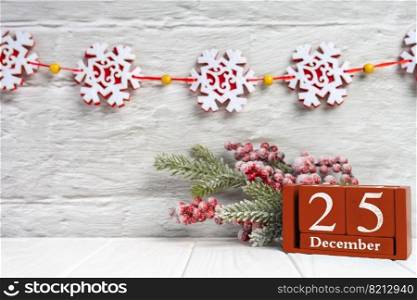 Christmas tree branch with red berries and red perpetual calendar with date 25 december on white brick wall with snowlakes garland. Banner, header, New Year background