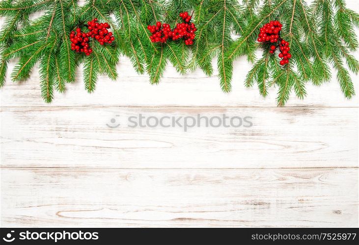 Christmas tree branch with red berries on wooden background. Winter holidays decoration