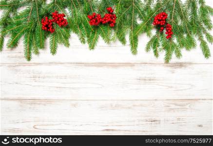 Christmas tree branch with red berries on wooden background. Winter holidays decoration