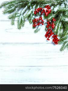 Christmas tree branch with red berries on wooden background. Winter holidays decoration. Retro toned, cold colors