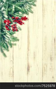 Christmas tree branch with red berries wooden background. Festive decoration. Winter holidays. Vintage style toned picture