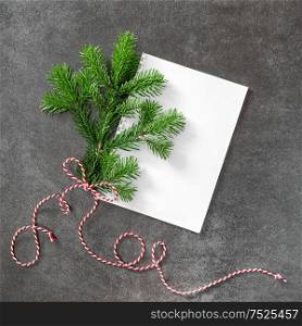 Christmas tree branch with white papaer on dark background. Minimal flat lay