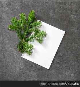Christmas tree branch with white papaer on dark stone background. Flat lay