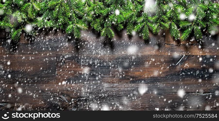 Christmas tree branches on dark wooden texture. Winter holidays background with falling snow effect