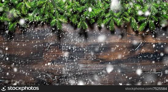 Christmas tree branches on dark wooden texture. Winter holidays background with falling snow effect