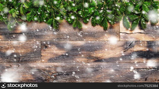 Christmas tree branches on rustic wooden background. Winter holidays background with falling snow effect