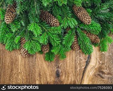 Christmas tree branches with cones on wooden background. Undecorated evergreen twigs