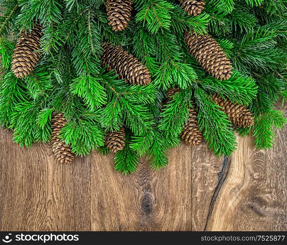 Christmas tree branches with cones over wooden background. Green border from undecorated evergreen twigs