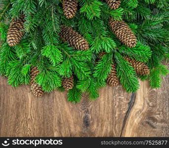 Christmas tree branches with cones over wooden background. Green border from undecorated evergreen twigs