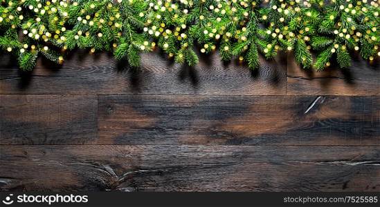 Christmas tree branches with golden lights on dark wooden background