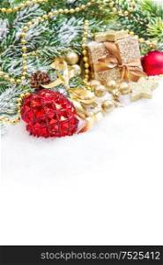 Christmas tree branches with red baubkle and golden gift box on white snow background