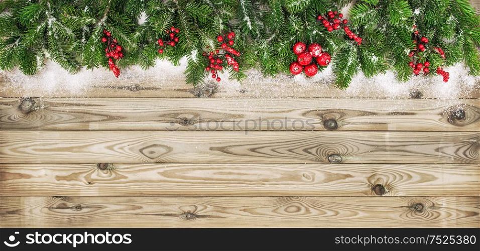 Christmas tree branches with red berries and snow decoration on wooden texture. Winter holidays background