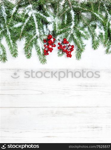 Christmas tree branches with red berries decoration and snow on wooden background