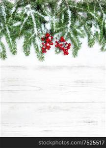 Christmas tree branches with red berries decoration and snow on wooden background