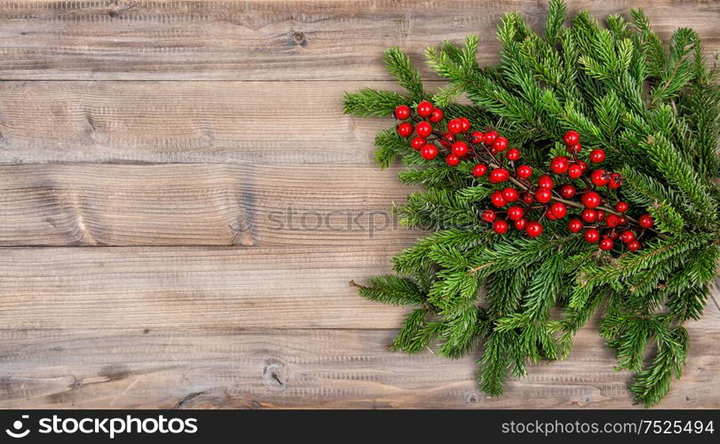 Christmas tree branches with red berries on wooden background. Festive decoration