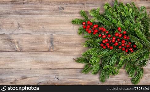 Christmas tree branches with red berries on wooden background. Festive decoration