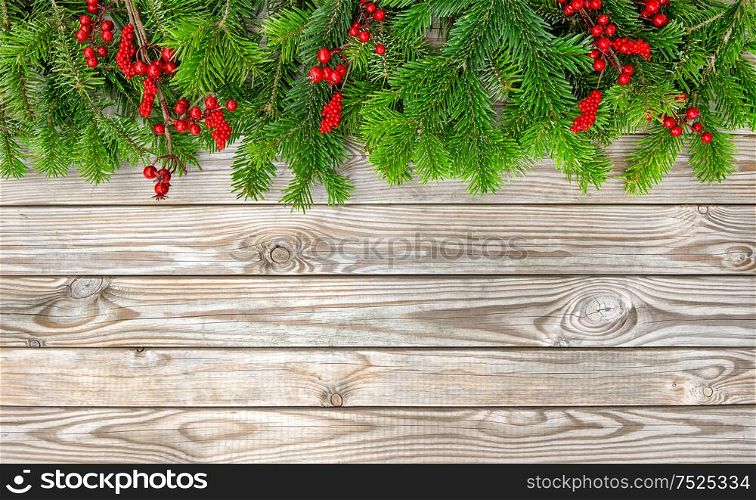 Christmas tree branches with red berries on wooden background. Winter holidays decoration