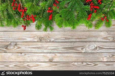 Christmas tree branches with red berries on wooden background. Winter holidays decoration