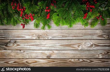 Christmas tree branches with red berries on wooden background. Winter holidays decoration. Vintage style toned picture with vignette