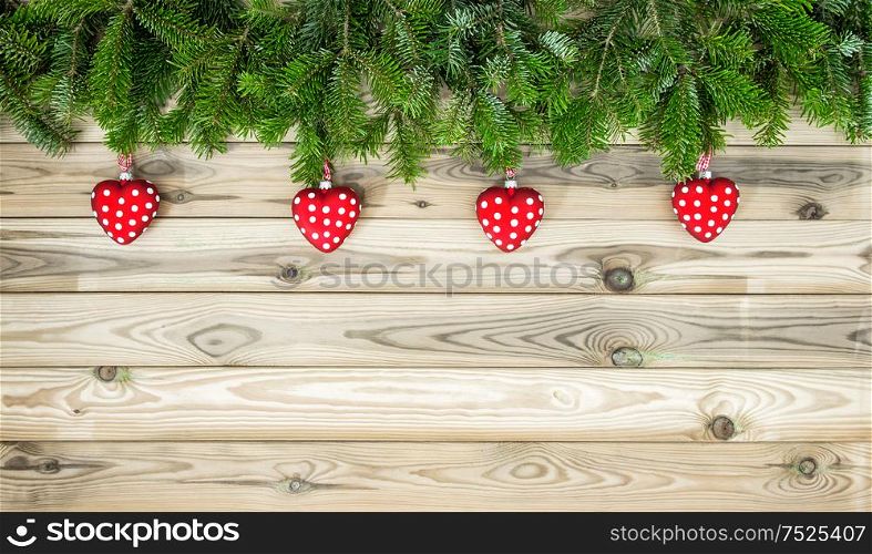 Christmas tree branches with red hearts baubles decoration on wooden texture. Winter holidays background