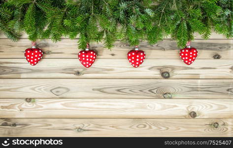 Christmas tree branches with red hearts baubles decoration on wooden texture. Winter holidays background