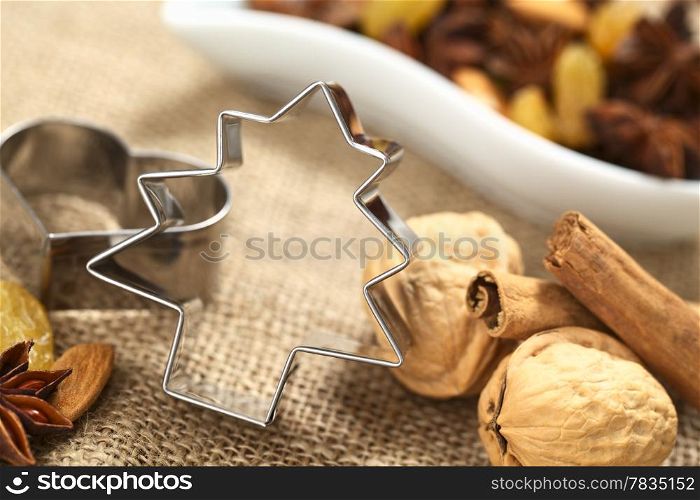 Christmas tree cookie cutter with other baking ingredients (walnut, cinnamon, anise, raisin and almond) (Selective Focus, Focus on the upper part and right side of the cookie cutter) . Tree Cookie Cutter with Baking Ingredients