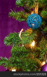 Christmas Tree decorated in a purple theme with a prominent blue ball and candle lights in sight