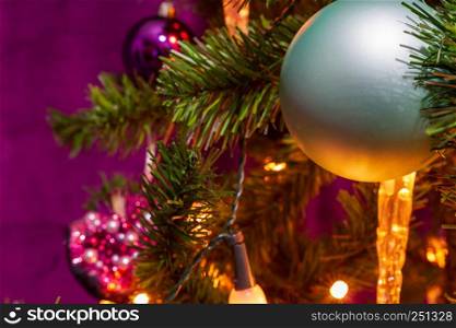 Christmas Tree decorated in a purple theme with a prominent cyan ball and a candle light in sight in the foreground