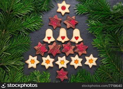 Christmas tree from homemade linzer cookies with raspberry jam and chocolate stars with raspberry crunches on slate table with pine branches. Christmas tree from homemade cookies on slate table with pine branches