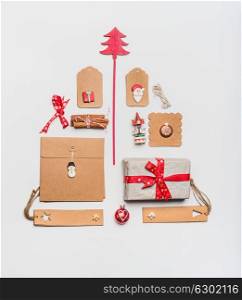 Christmas tree layout made with craft paper wrapping gift boxes, tags, toys, red holiday decoration and spices on white desk background, top view, flat lay. Festive pattern for greeting card