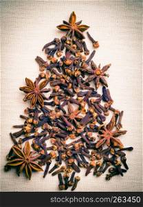 Christmas tree made from brown spices anise stars and cloves on burlap background