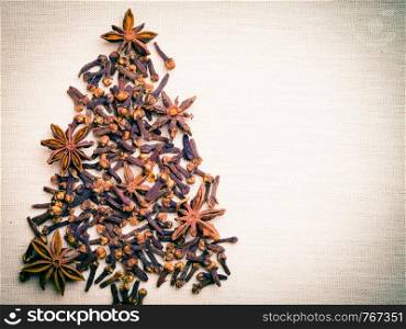Christmas tree made from brown spices anise stars and cloves on burlap background