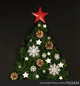 Christmas tree made of natural spruce branches deecor with red star on black background, flat lay card with copy space. Christmas tree card