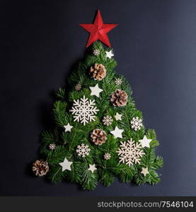 Christmas tree made of natural spruce branches deecor with red star on black background, flat lay card with copy space. Christmas tree card