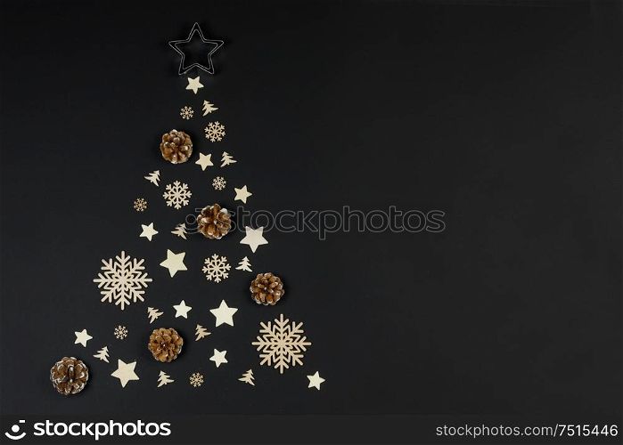 Christmas Tree made of wooden decor and pine cones on black paper background. Christmas Holiday Concept. Flat Lay. Christmas Holiday Concept